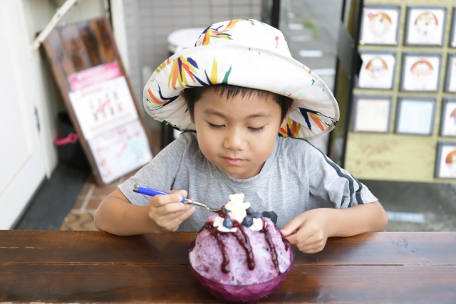 紫色のかき氷を食べている帽子を被った子供
