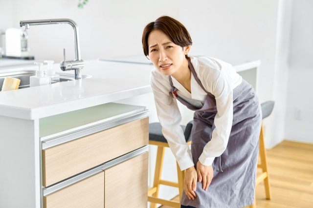 膝を抑えるエプロン姿の女性